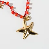 Collar corto con cadena de hilo rojo con cuentas de color coral y dijes colgantes de estrella de mar y pez en color dorado.