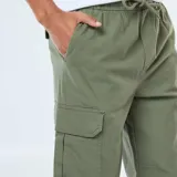 Pantalón cargo de hombre color verde militar, con múltiples bolsillos laterales y puños ajustados elásticos en los tobillos. Presenta cintura elástica con cordón de ajuste.