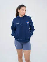 Canguro azul marino con capucha y cordones ajustables, bolsillo frontal tipo canguro, mangas largas y costuras visibles en contraste claro. Incluye el logo de Umbro y el escudo del Club Nacional de Football bordados en el frente.