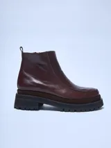Bota de caña baja de cuero color marrón oscuro, con puntera cuadrada y suela track gruesa de goma negra. Presenta un panel de gamuza marrón entre la capellada de cuero y la suela.