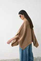 Capita de tejido de punto grueso en color camel, con cuello alto tipo polera y diseño holgado con aberturas laterales para los brazos.