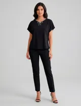 Blusa de modal suave color negro, con mangas cortas y corte holgado. Presenta un escote redondo decorado con una línea de strass y un broche desmontable en forma de moño con strass en el centro. La espalda cuenta con una abertura tipo gota con cierre de botón.