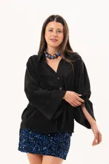 Camisa negra plisada de manga larga con puños vueltos, cuello camisero y cierre frontal de botones claros.