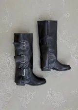 Botas de caña alta confeccionadas en ecocuero negro, con diseño de tres hebillas metálicas laterales y suela plana.