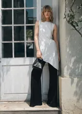 Bolso de mano pequeño con diseño estructurado y minimalista en color negro. Presenta un asa superior rígida de metal dorado y cuerpo de material sintético con acabado texturizado.