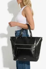 Cartera shopper de cuero vegano negro, de diseño estructurado, con doble bolsillo frontal con cierre y tiradores colgantes. Cuenta con asas dobles de mano y una correa regulable extraíble para usar al hombro o cruzada.