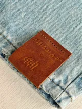 Jean de corte wide leg en denim azul claro, intervenido a mano con ilustraciones abstractas de rostros en líneas color rosa y blanco. Presenta tiro medio-alto y diseño de cinco bolsillos.