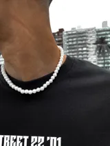 Collar de perlas blancas con dije de cruz plateada incrustado con zirconias, con terminaciones en acero inoxidable.