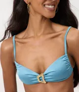 Top de bikini bandeau celeste con acabado satinado, breteles finos y un llamativo aplique metálico dorado en el centro.