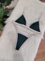 Conjunto de lencería compuesto por bralette triangular y tanga, confeccionado en algodón color verde inglés con detalles de encaje en tono nude. El bralette cuenta con breteles ajustables y broche regulable, mientras que la tanga presenta laterales ajustables.