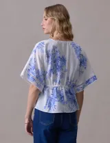 Blusa blanca estampada con flores azules, escote en V y mangas cortas amplias. Detalles de puntilla en escote y mangas.