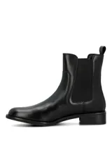 Bota tipo Chelsea de cuero negro, con paneles elásticos laterales y tirador en la parte trasera. Presenta un diseño de caña media con suela plana y taco bajo cuadrado.