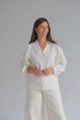 Blusa de color crudo con cuello mao y cierre frontal de botones. Presenta mangas largas abullonadas con puños y un delicado diseño bordado con relieve en toda la prenda.