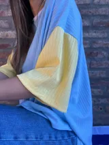 Remera de corte oversize confeccionada en tejido de punto acanalado color celeste, con mangas cortas en color amarillo y detalle de parche bordado con la bandera de Uruguay en la parte superior de la espalda.