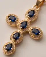 Collar con dije de cruz de bronce con baño de oro y piedras ovaladas color azul.
