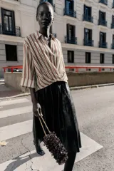 Camisa de cuello solapa con escote en pico, manga tres cuartos con vuelta y bajo asimétrico con pliegues delanteros que generan un efecto abullonado.