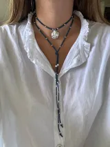 Collar de cuero azul con dije plateado en forma de caracol y detalles de cuentas plateadas. El collar tiene dos tiras que caen por el frente.