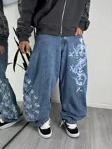 Pantalón jean baggy de corte holgado y tiro medio en color azul, con diseño bordado de flores y estampado de dragón con caracteres orientales en las piernas.