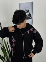 Campera canguro con cierre frontal, de color negro, con diseño estampado de ramas de cerezo en flor a un lado y sobre el hombro.