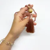 Japa Mala elaborado con 108 cuentas de rodonita de 6 mm de diámetro, dije gurú de madera y borla de hilo de seda color beige. Incluye guía de meditación con mantras.