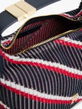 Cartera tipo hobo de Tommy Hilfiger con diseño de rayas diagonales en azul marino, rojo y blanco. Presenta un asa superior fija, una correa ajustable extraíble, cierre superior y el logo metálico TH en la parte frontal.