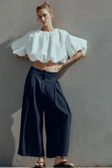 Pantalón tipo culotte de tiro alto confeccionado en denim azul oscuro. Presenta pinzas delanteras, pernera ancha y corta, bolsillos laterales ocultos y cierre frontal con cremallera, botón y ganchos.