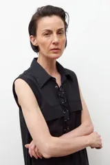 Vestido corto color beige, sin mangas, con cuello camisero, cierre frontal con cordones cruzados y múltiples bolsillos con cierre.