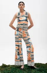 Pantalón de denim con estampado psicodélico en tonos naranja, celeste y negro. Presenta un corte recto o ligeramente acampanado con dobladillo ancho en el ruedo.