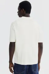 Camisa de punto acanalado color blanco, con cuello camisero, manga corta y cierre frontal con botones.
