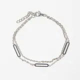 Pulsera de doble cadena de eslabones finos en color plateado, con tres dijes rectangulares alargados integrados en el diseño. Cuenta con cierre de mosquetón y cadena de alargue.