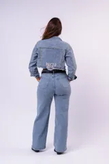 Campera de jean cropped con tachas plateadas distribuidas en el frente, hombros y mangas. Presenta un diseño con bordes deshilachados, cuello clásico y cierre frontal con botones metálicos.