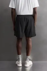 Pantalones cortos negros de tejido técnico perforado, ligeros y elásticos. Cuentan con cintura elástica ajustable con cordón interior, bolsillos frontales, bolsillo trasero de seguridad con cierre de cremallera, perneras con laterales perforados para transpirabilidad, bajo con acabado termofijado y aberturas laterales. Incluye detalle de logo estampado en la pernera.