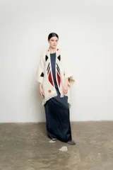 Ruana de tejido grueso color crudo, con flecos en el ruedo y diseño geométrico en negro, bordó y blanco.