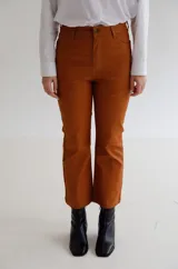 Pantalón cropped de tiro medio con acabado engomado, corte recto y bolsillos laterales. Presenta cierre frontal con botón y costuras a tono.