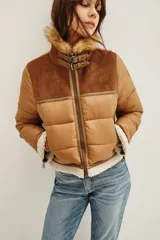 Campera estilo aviador en tonos tostados, con diseño acolchado y paneles de gamuza en la parte superior. Presenta cuello alto con doble hebilla, cierre frontal completo y detalles de corderito sintético en el cuello y el ruedo.