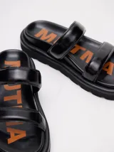 Sandalias de cuero vacuno color marrón con acabado brillante, diseño de dos tiras anchas acolchadas y plataforma baja.