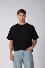 Remera boxy negra de algodón peinado esmerilado, con cuello redondo y mangas cortas, presenta un pequeño texto estampado en el pecho.