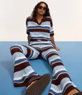 Pantalón femenino de punto con efecto crochet, de corte flare, cintura elástica y rayas horizontales en diferentes anchos y colores (azul claro, azul medio, bordó y blanco).