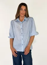 Camisa de lino color celeste, con cuello camisero, cierre frontal con botones y mangas abullonadas tres cuartos.