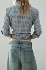 Jeans de tiro medio con cinco bolsillos, trabillas y cierre frontal con cremallera y botón metálico. Presenta un diseño baggy con piernas anchas, roturas decorativas y dobladillo vuelto en los bajos.