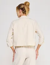 Blazer corto de lino color beige, marca Allie Rose, de estilo relajado y corte crop con frente abierto sin botones. Presenta solapa de muesca y mangas tres cuartos con detalle fruncido en los laterales.