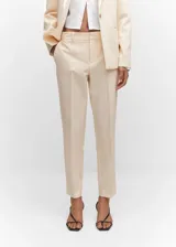 Pantalon de vestir de corte recto y tiro medio, confeccionado en tejido fluido color beige. Presenta trabillas en la cintura, dos bolsillos laterales y dos bolsillos de ribete en la parte posterior.