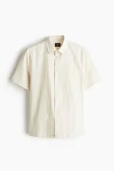Camisa de manga corta H&M con cuello inglés, cierre frontal de botones y bolsillo en el pecho. Presenta un diseño de rayas verticales sutiles en tejido de mezcla de algodón.
