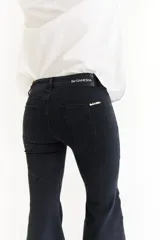 Jean de corte oxford con tiro medio, confeccionado en denim negro. Presenta recortes curvos en las piernas y detalle de botones metálicos en los laterales de la botamanga.