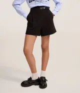 Short sastre de corte recto y cintura alta color verde militar, con pinzas delanteras, trabillas para cinturón y cierre frontal oculto. Incluye un medio cinturón lateral de poliuretano con hebilla.