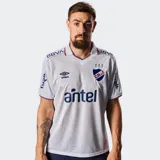 Camiseta de fútbol Umbro del Club Nacional de Football, modelo Home 2026. Diseño en color blanco con detalles en azul y rojo en el cuello y puños. Presenta un patrón jacquard sutil en toda la prenda, el escudo del club, el logo de Umbro y el sponsor Antel en el frente.