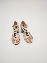 Sandalias de tacón cuadrado de 8 cm, confeccionadas en charol color crema. Presentan un diseño de tiras finas entrelazadas en la parte frontal y una correa ajustable con hebilla metálica en el tobillo.