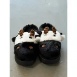 Pantuflas de peluche con diseño de vaca, confeccionadas en piel sintética suave. Cuentan con suela de goma antideslizante y diseño abierto en el talón.