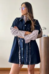 Vestido corto de jean azul oscuro, sin mangas, con cierre frontal de botones metálicos y corte ligeramente evasé.
