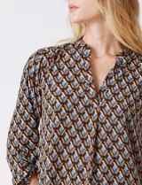 Blusa de gasa estampada con patrón geométrico en tonos azul, marrón y amarillo. Cuello a la base con detalle plisado y escote en V. Manga larga con presilla y botón para regular el largo.